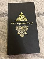 Front cover of the Hiponymous collector box set by The Tragically Hip showing black hardcover with gold embossed band name and symbol