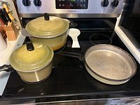 Full set of two pots with lids and one frying pan on stove; visible oxidation on pot bottoms and pan surface