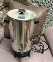 Stainless steel coffee urn with black handles, lid with knob, black spigot at base, showing overall physical condition and design.