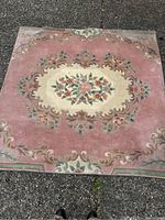 Square pink and white area rug laid on outdoor pavement showing floral pattern with finished edges.