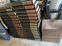 Photo showing multiple stacks of Encyclopaedia Britannica volumes with clearly visible spines marked with titles and volume numbers.