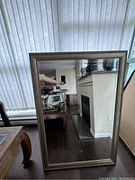 Large rectangular mirror in bronze-colored frame standing vertically reflecting room interior