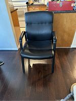 Front view of black leather office chair with high back and padded armrests on wooden floor.