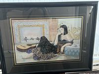 Framed picture showing a seated woman in black dress next to an acoustic guitar, with glass cover reflecting light.