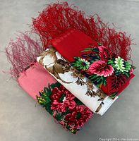 Three vintage woolen Persian shawls stacked, showing red, pink, and white colors with floral designs and fringes