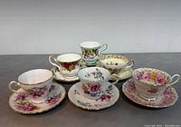 Front view of six bone china teacups with matching saucers showing varied floral patterns and gold rims.