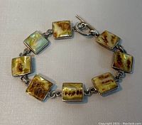 7.25 inch sterling silver bracelet laid flat showing seven square stones with brown, cream, and green marbled patterns. Toggle clasp visible.