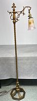 Full view of the floor lamp showing twisted metal pole and ornate metal base with lamp arm and pulled feather art glass shade.