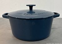 Front angle view of blue enameled cast iron casserole with lid on, showing side handles and lid knob.