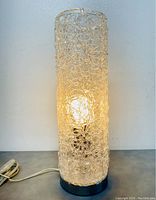 Lamp illuminated showing warm light through clear textured patterned glass shade on metal base.