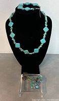 Front view of turquoise necklace displayed on black bust with earrings on clear acrylic stand below.