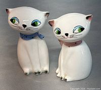 Front view of the two Siamese cat salt and pepper shakers showing white ceramic with blue and pink scarves and green eyes