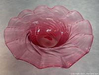 Angled view showing ruffled edge, spiral swirl pattern, and cranberry red color of the glass bowl.