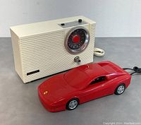 Photo of Panasonic vintage radio and Porsche red landline phone together on grey surface.