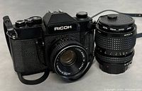 Front view of Ricoh film camera with attached Auto Rikenon 50mm lens and separate Minolta 55mm UV(1) lens.
