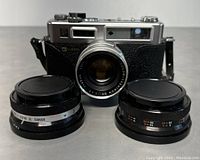 Front view of Yashica Electro 35 camera body with attached Color Yashinon DX 45mm f/1.7 lens and two additional lenses laid in front