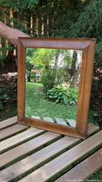 Full front view of rectangular wood framed mirror placed outdoors showing reflection of greenery and sky