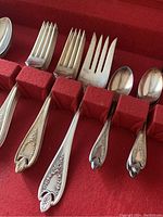 Close-up of various ornate silverplate cutlery handles and utensils placed in a red felt organizer.