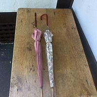 Two closed umbrellas with pink and floral canopies on wooden table, showing overall condition and length.