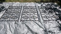 Three black wrought iron room divider panels laid flat on tarp outdoors, showing front side with butterfly design in circles.