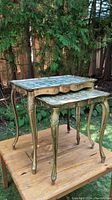 Pair of Florentine style nest tables shown outdoors on a wooden table under trees.