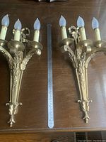 Pair of Beaux Arts solid brass wall sconces laid on wooden table with measuring ruler showing length around 18 inches.
