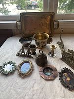 Wide shot of lot showing all items on white fabric, including brass tray, bowls, candle holders, letter rack and small frames