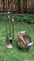 Overall view of brass fireplace accessory set on grass showing coal scuttle, tapper holder, and fireplace tool set with stand