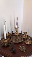 Photo showing all candlesticks including paired and individual brass candlesticks and steel lotus flower holders on a wooden surface.