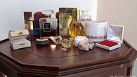 Wide view of all items grouped on wooden octagonal table showing perfume bottles, powder jar, jewelry boxes, scarf hanging in background.