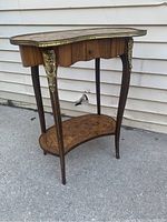 Full view of French boudoir style lamp table showing curved legs, kidney-shaped wooden top with brass rail, lower inlaid shelf, and drawer.