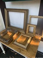 Full set of five antique gilt picture frames with varying sizes and styles, laid on wooden table.