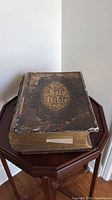 Full view of large leather-bound Bible with worn cover and visible gold embossing with 'The Holy Bible' text on front.