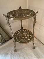 Front view of entire two-tier brass trivet table showing top and bottom shelves, legs, and overall form