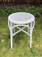 Front view of white wicker round stool with woven seat on grass.