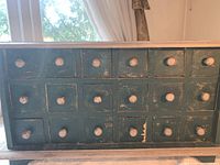 Front view showing 18 small drawers arranged in three rows of six, each with a single round wooden knob. Distressed paint finish visible.
