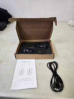 Two black wireless units (transmitter and receiver) with gold 1/4 inch plugs in foam inside a cardboard box, USB charging cable, and instruction manual on table.