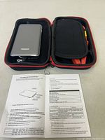 Compact silver power bank and cables in zippered black and red case with user manual