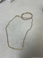 Photo of a gold plated stainless steel chain necklace approximately 55 cm long along with a matching bracelet coiled near the necklace chain.