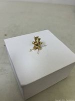 Gold teddy bear pendant resting on a white box, showing front side detail.