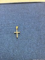 Front view of a small gold cross pendant with clear stones set on the front surface.