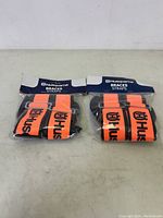 Two sealed sets of orange Husqvarna braces straps with black branding in original packaging, shown side by side.