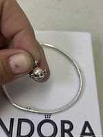 Hand holding the Finding Nemo charm with the coiled silver-tone snake chain bracelet displayed on a white Pandora box, showing the charm's facial details and orange stripes