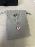 Overall view of the silver necklace on a grey pouch, displaying pendant size and chain style.