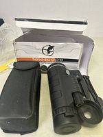 Foldable black monocular telescope, tripod stand, carrying case, and original box shown on surface.