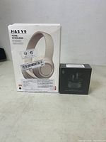 Two boxed items on table: H&S V9 wireless headset box and Lucifer Black Shark T2 earbuds box.