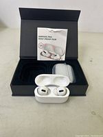 Apple AirPods Pro earbuds in open charging case with dust-proof film pack and black box background