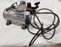 Full view of the air compressor unit showing the metal body, motor, pressure gauge, control valves, and attached multi-colored air hose with connector.