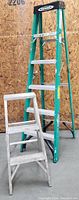 Front view of the two ladders against plywood wall showing Werner fiberglass A-frame ladder and smaller aluminum ladder