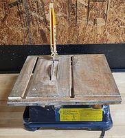 7 inch wet tile saw with a metal table showing rust and a yellow blade guard.